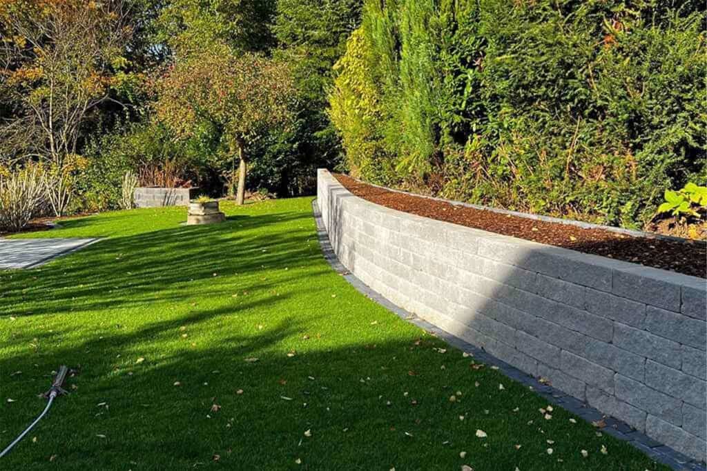 Garten mit geschwungener Stützmauer und frischem Rasen