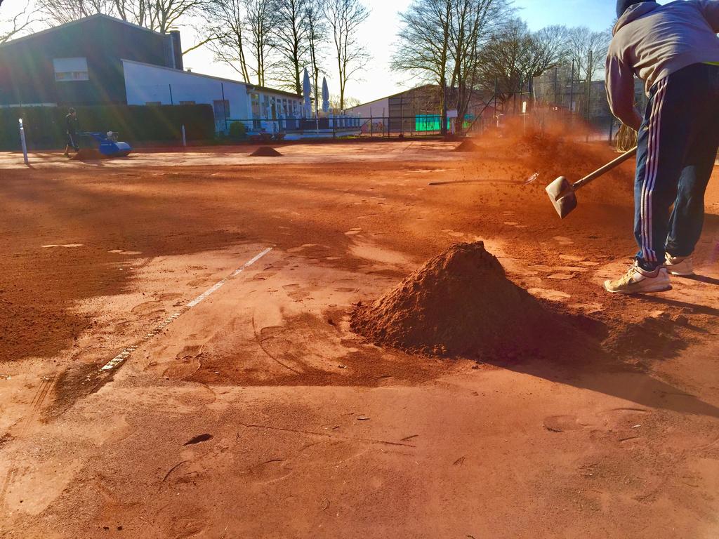 Mitarbeiter verteilt Ziegelmehl auf einem Tennisplatz